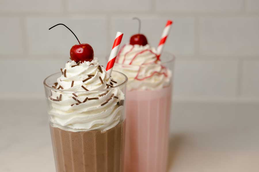 two faux milkshakes topped with whipped cream, sprinkles, and cherries 