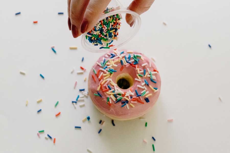 a hand sprinkling faux sprinkles onto a faux doughnut