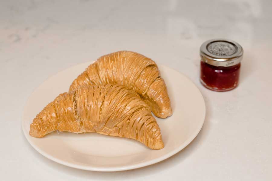two faux croissants on a plate and a small jarof faux jam